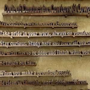 May include: A wooden plaque with a carved design and the text "Code of Conduct for Cowboys & Cowgirls". The plaque lists ten rules of conduct, including "Take pride in your work, always do your best", "Stay curious, Study hard and learn all you can", and "Be an excellent steward of the land and its animals".
