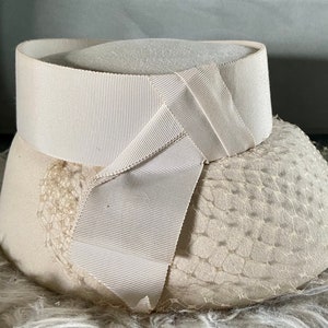 May include: A white hat with a wide brim and a white ribbon tied around the crown. The hat is made of a soft, textured fabric and has a delicate netting detail.