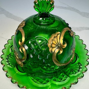 May include: A green glass butter dish with a domed lid and a scalloped edge base. The lid features a decorative gold-colored handle and gold-colored accents. The glass has a diamond pattern and gold embellishments. A decorative serving dish.
