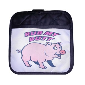 May include: A black quilted pot holder with a white panel featuring a pink pig with the text "RUB MY BUTT" in pink and blue letters.