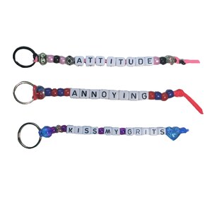 May include: Three keychains with colorful beads and white letter tiles spelling out "ATTITUDE", "ANNOYING", and "KISS MY GRITS".