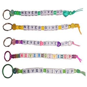 May include: Five colorful beaded keychains with the phrase "NEVER GIVE UP" spelled out in white letter beads. Each keychain has a different color scheme and charm.