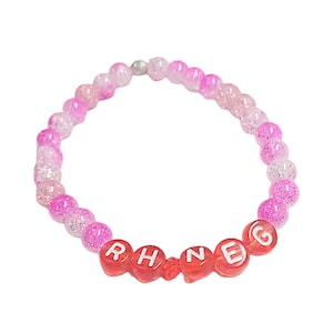 May include: A pink and white ombre beaded bracelet with the name "RHNEG" spelled out in red beads.