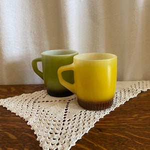 May include: Two vintage ceramic mugs with a brown rim. One mug is green and the other is yellow.