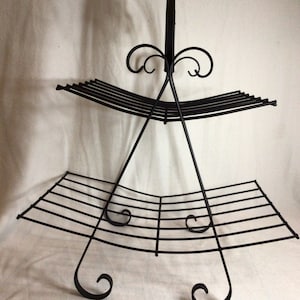 May include: Black metal magazine rack with two tiers and decorative scrollwork. The rack is designed to hold magazines or books.