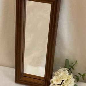 May include: A rectangular wall mirror featuring a dark brown wooden frame with a stepped, tiered profile. The mirror glass is clear and reflective, set within the deep, structured border of the wood frame, which has a smooth, polished finish.