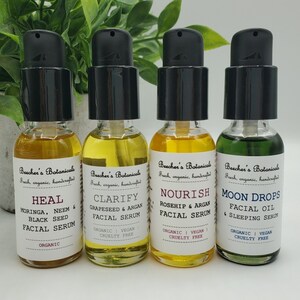 May include: Four glass bottles with black pump tops containing facial serums and oils. The bottles are labeled with the brand name "Beecher's Botanicals" and the product names "Heal", "Clarify", "Nourish", and "Moon Drops".