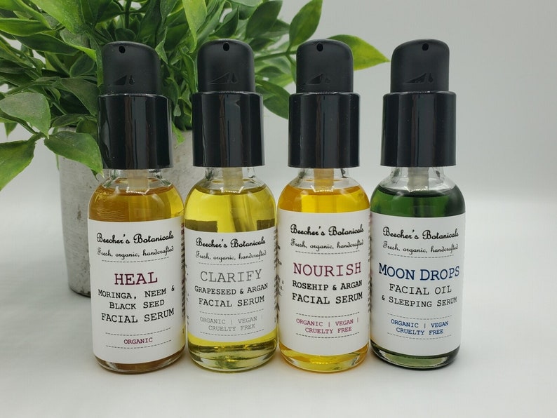 May include: Four amber glass bottles with black pump tops and white labels. The labels have the text "Beecher's Botanicals" and list different facial serums: "Heal", "Clarify", "Nourish", and "Moon Drops".