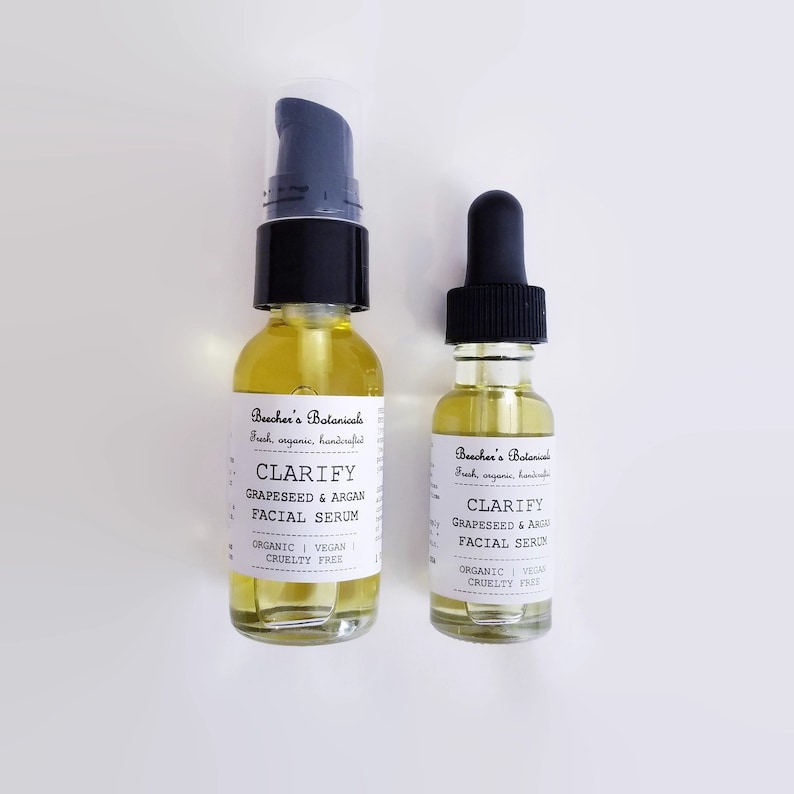 May include: Two glass bottles of facial serum with black pump tops and droppers. Both bottles have white labels with the text "Beecher's Botanicals" and "Clarify GrapeSeed & Argan Facial Serum". The labels also state "Organic | Vegan | Cruelty Free".