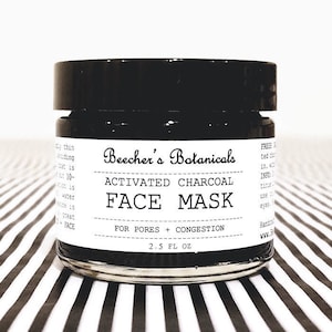 May include: A black jar with a white label that reads "Beecher's Botanicals Activated Charcoal Face Mask For Pores + Congestion 2.5 FL OZ".