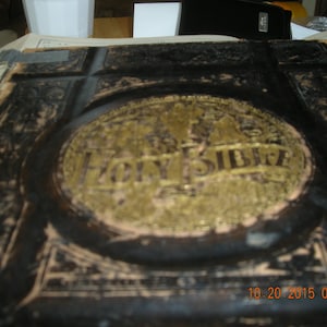 May include: A worn, black leather-bound book with a gold embossed title, "HOLY BIBLE", on the front cover.