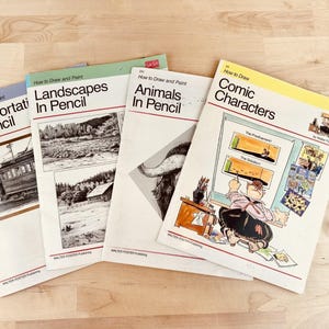 Könnte beinhalten: Vier Vintage-Zeichenbücher mit den Titeln "Transportation In Pencil", "Landscapes In Pencil", "Animals In Pencil" und "Comic Characters". Die Bücher haben weiße Umschläge mit Illustrationen und Text. Auf einer hellen Holzoberfläche.