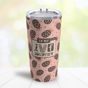 Puede incluir: Un vaso de acero inoxidable rosa con un patrón de piña marrón y el texto "On my IVF Journey".