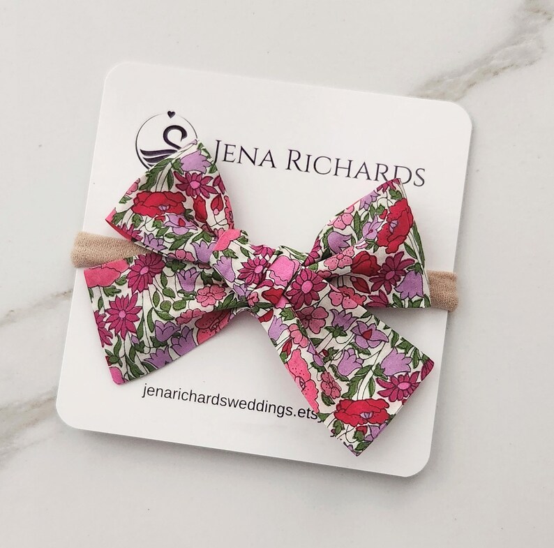 Baby bow headband in the sweet Liberty London Poppy Forest pink and purple floral print on a nylon band.