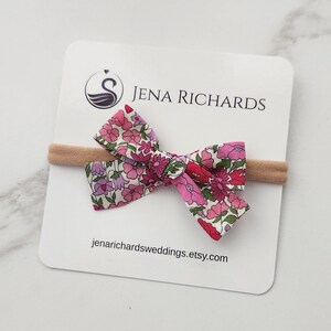 A small 2.5 inch floral hair bow for infants and newborn baby girls in a sweet pink and purple Liberty London Poppy Forest print on a nylon band