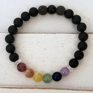 May include: A black beaded bracelet with seven colorful gemstone beads and two clear spacer beads. The bracelet is made with black lava rock beads and black onyx beads.