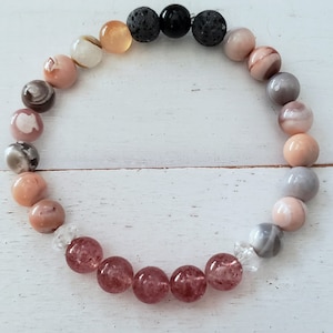 May include: A multi-colored beaded bracelet with pink, orange, white, gray, and black beads. The bracelet is made with natural stones and lava beads.