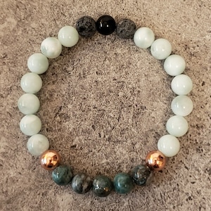 May include: A bracelet made of white, green, and black beads with copper accents. The bracelet has a mix of round and irregular shaped beads.