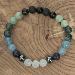 May include: A beaded bracelet with a gradient of green, blue, and white stones. The bracelet also includes black lava rock and hematite beads.