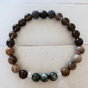 May include: A brown, black, and green beaded bracelet with a variety of stones, including clear quartz, tiger's eye, and lava rock.