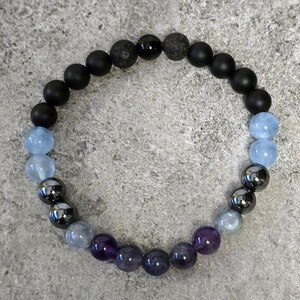 May include: A beaded bracelet with black, blue, and purple beads. The bracelet is made with lava rock, amethyst, aquamarine, and hematite beads.