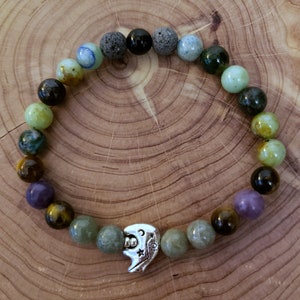 May include: A beaded bracelet with a variety of green, brown, black, and purple stones. The bracelet has a silver charm in the shape of a crescent moon with a star.