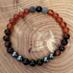 May include: A beaded bracelet with a gradient of orange, brown, black, and gray beads. The bracelet is made with carnelian, tiger's eye, black onyx, and hematite beads.