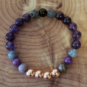May include: A purple, blue, and black gemstone bracelet with copper beads. The bracelet is made with amethyst, lava rock, and other stones.