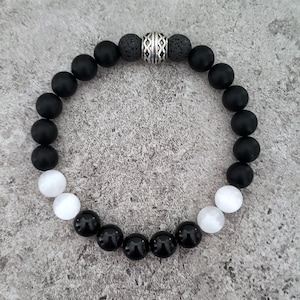May include: Black and white beaded bracelet with a silver spacer bead. The bracelet features black onyx, white moonstone, and lava rock beads.