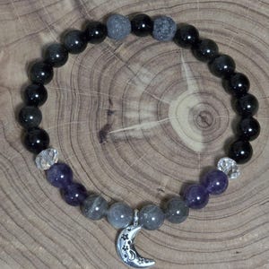 May include: A beaded bracelet featuring black, gray, and purple gemstones. The bracelet includes a silver crescent moon charm with star cutouts. The beads are strung together, creating a stylish accessory.