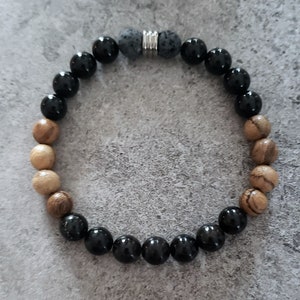 May include: A black and brown beaded bracelet with a silver metal clasp. The bracelet has a mix of black, brown, and grey beads.