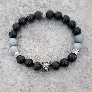 May include: A black and grey beaded bracelet with a silver wolf charm. The bracelet features a mix of black onyx, grey lava rock, and grey agate beads.