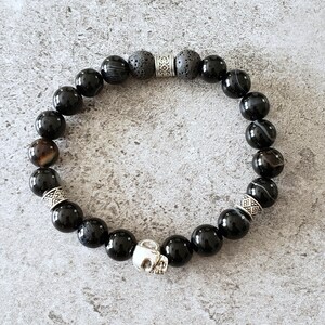 May include: Black onyx and lava rock beaded bracelet with silver skull charm and decorative spacers.