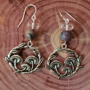 May include: Silver earrings with a mushroom design, featuring a clear crystal and a purple and grey stone.