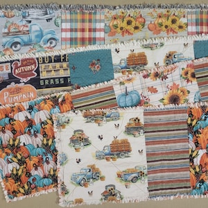 May include: A rag quilt featuring a patchwork design with various autumn-themed fabrics. Patterns include blue vintage trucks carrying pumpkins, sunflowers, plaid stripes, and text reading "Autumn," "Farm," and "Golden Pumpkin" with frayed edges.