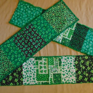 May include: Green shamrock patterned table runner with a fringed edge. The runner is made of fabric and is perfect for a St. Patrick's Day celebration.