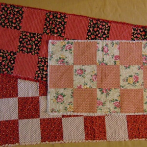 May include: Three red and white patchwork table runners with different patterns. The top runner has a black and white floral pattern, the middle runner has a floral pattern, and the bottom runner has a checkered pattern.