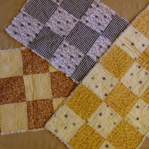 May include: Three handmade quilted table runners in different patterns. The first runner is a black and white checked pattern with a floral design. The second runner is a yellow and brown checked pattern with a floral design. The third runner is a yellow and white checked pattern with a bee design.