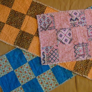 May include: Three patchwork table runners with a checkered pattern. The first runner is brown and orange, the second is pink and white, and the third is blue and white.