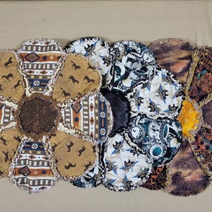 Könnte beinhalten: Ein handgefertigter, blütenförmiger Flickenteppich mit verschiedenen gemusterten Stoffen. Der Quilt zeigt Pferde-, geometrische und abstrakte Designs in Braun-, Blau- und Cremetönen. Die Mitte ist ein dunkelbrauner, strukturierter Stoff.