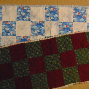 May include: Two patchwork quilt table runners. The top runner is white with blue and red squares with a cloud pattern. The bottom runner is a checkerboard pattern of dark red and green squares.