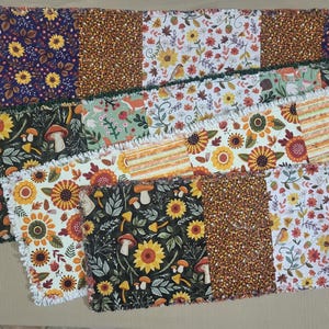 May include: A rectangular rag quilt table runner featuring a patchwork design of various autumn-themed fabrics. The patterns include yellow sunflowers on dark backgrounds, orange and brown floral prints, mushrooms, and small birds on white fabric.