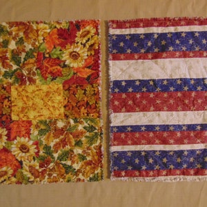 Puede incluir: Dos manteles individuales de tela con borde deshilachado. Un mantel individual tiene un tema otoñal con un diseño de patchwork de hojas, girasoles y bellotas. El otro mantel individual tiene un diseño a rayas rojo, blanco y azul con estrellas.