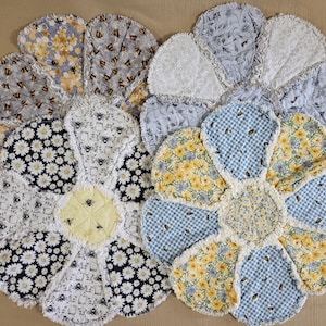 May include: Four handmade, flower-shaped rag quilts. The quilts feature various floral and bee patterns in yellow, blue, white, and black. The petals have a frayed edge, and the centers are a contrasting color with bee details.