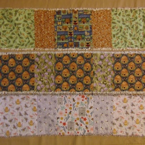 May include: Three fabric table runners with different patterns. The top runner has a green, orange, and blue pattern with a variety of small images. The middle runner has a brown, green, and purple pattern with a beehive design. The bottom runner has a white, purple, and yellow pattern with a bee and flower design.