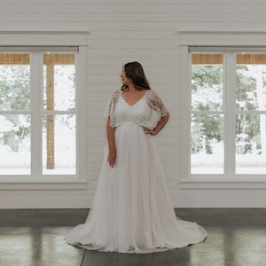May include: A white wedding dress with a lace bodice and a flowing skirt. The dress has a simple design and is perfect for a casual wedding.