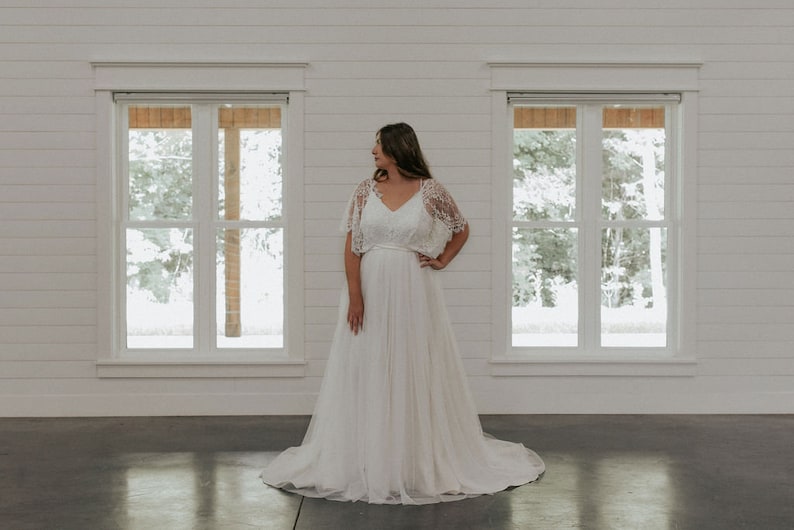 May include: A white wedding dress with a lace bodice and a flowing skirt. The dress has a simple design and is perfect for a casual wedding.