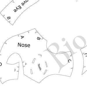 Puede incluir: Patrones de papel blanco con las palabras "Nose", "Tooth" y "Love Eye" impresas. Las piezas están etiquetadas con letras y tienen pequeñas marcas triangulares a lo largo de los bordes.