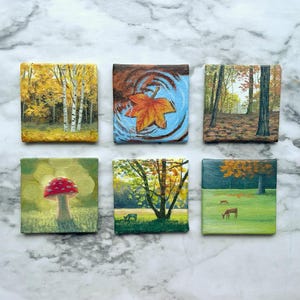 May include: Six small square canvases featuring detailed nature paintings. The top row shows a yellow birch forest, an orange maple leaf in blue water, and a forest path. The bottom row depicts a red mushroom, a tree in a field, and deer in a meadow.