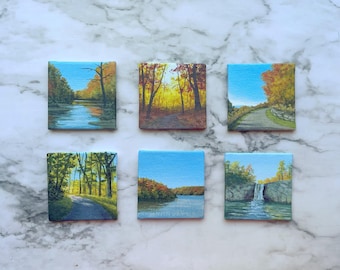 May include: Six square canvas paintings featuring landscape scenes. The top row shows a river, a sunlit forest path, and a winding road. The bottom row depicts a green forest trail, a calm lake with autumn foliage, and a small waterfall.